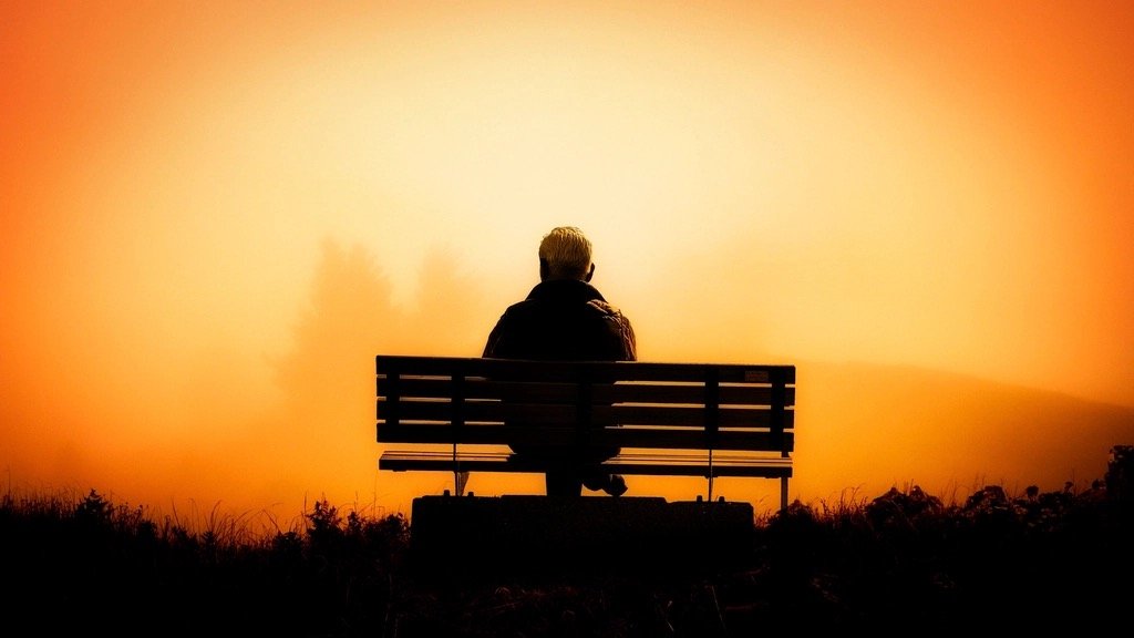 Silhouette of a person sitting on a bench, gazing into a golden dawn sky
