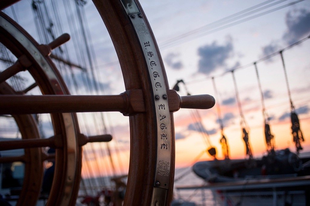 A wooden ship's wheel on deck at sunset