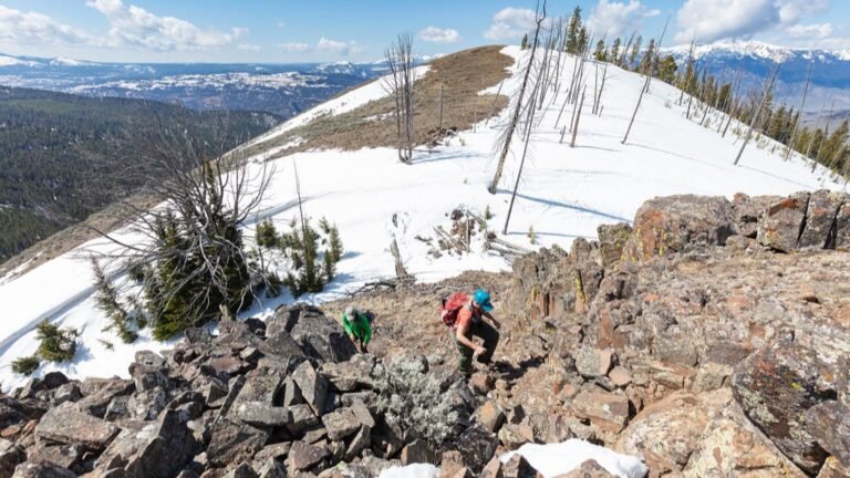 Two hikers climbing over rocky terrain on the final push to a mountain summit