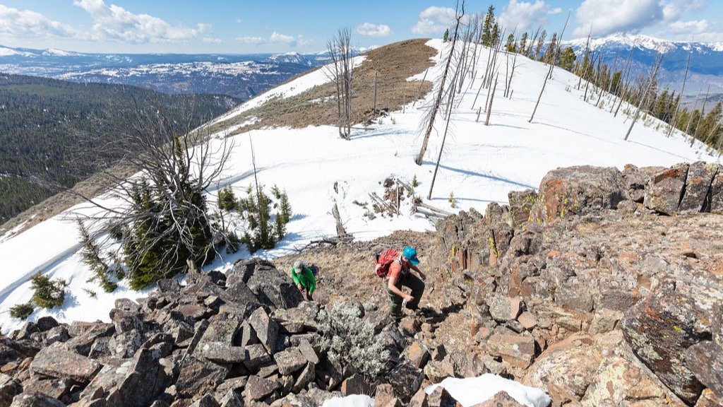Two hikers climbing over rocky terrain on the final push to a mountain summit