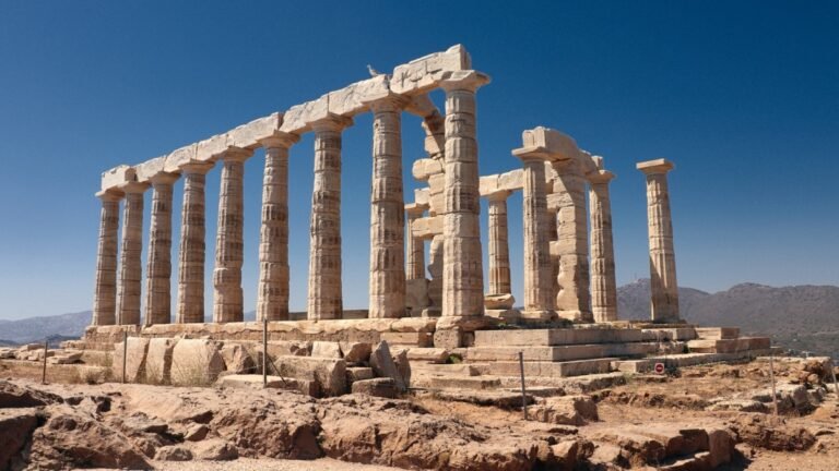 Ancient stone columns of a hilltop temple standing against a clear blue sky, with gaps where other columns have fallen