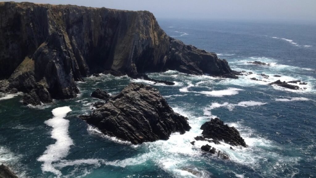 Waves breaking hard against dark rocks along a steep coastline