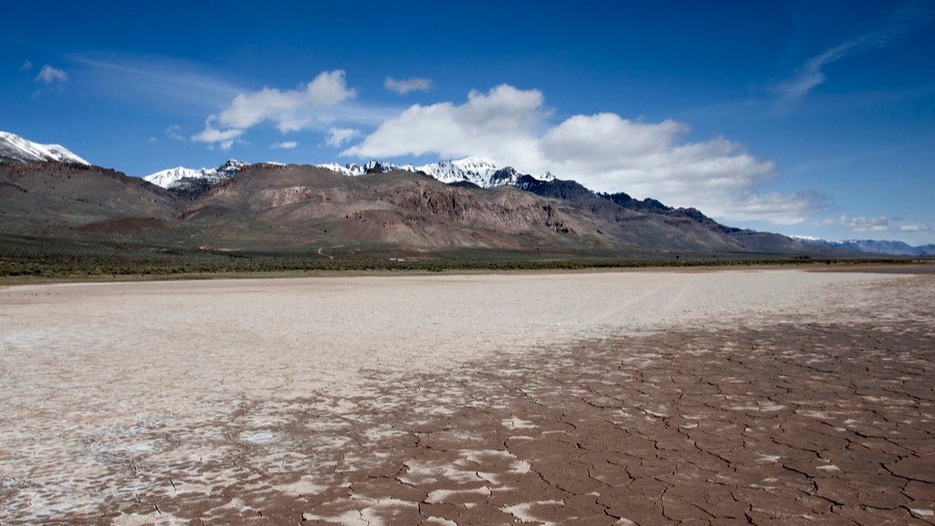 A dry cracked desert floor stretching toward distant snow-topped mountains