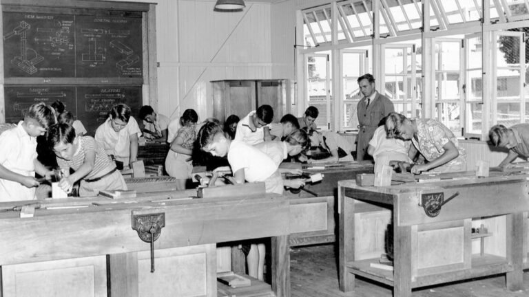 A workshop of people bent over benches working with hand tools